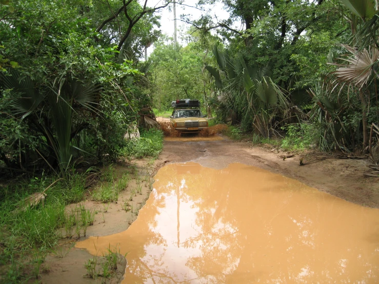 a muddy road with a vehicle driving in the dirt