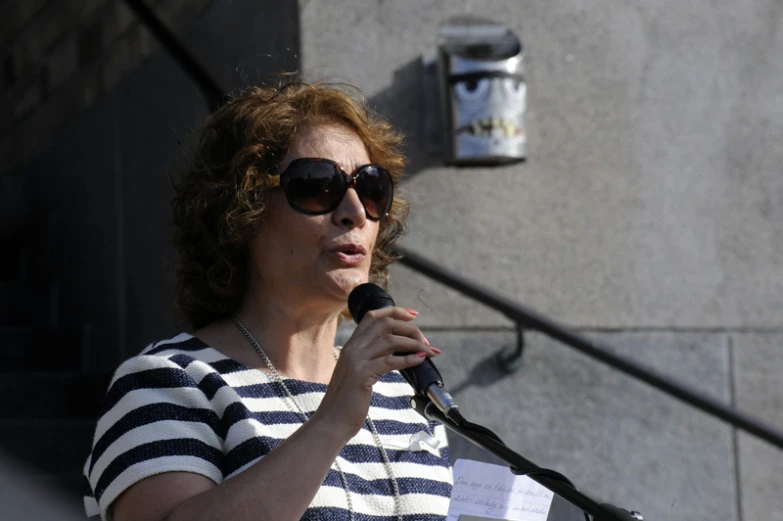 a woman with large sunglasses is speaking into a microphone