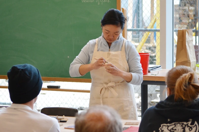 an asian woman wearing an apron standing in front of a class