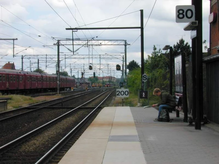 man sitting on a bench with a rail road track and train passing by