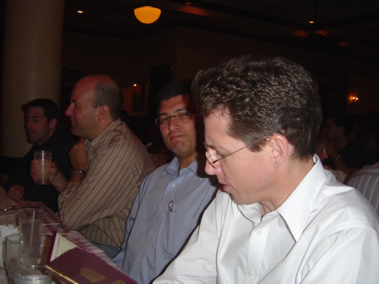 three men are sitting at a bar looking at a menu