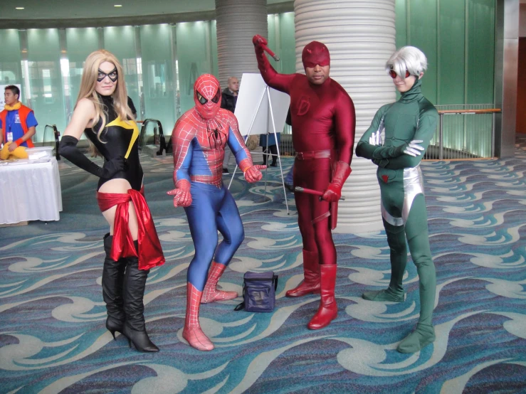 three people dressed as superheros standing in a convention hall