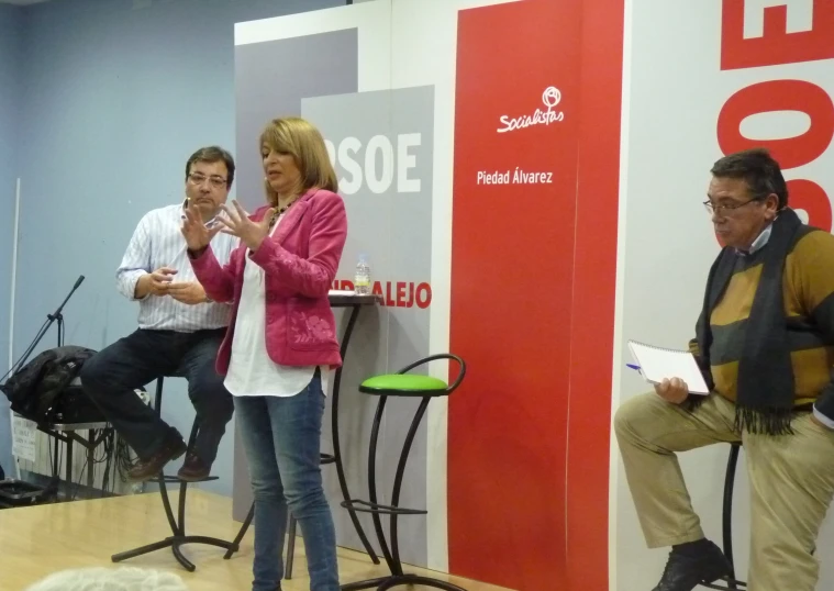 a woman in a pink blazer is speaking to two people