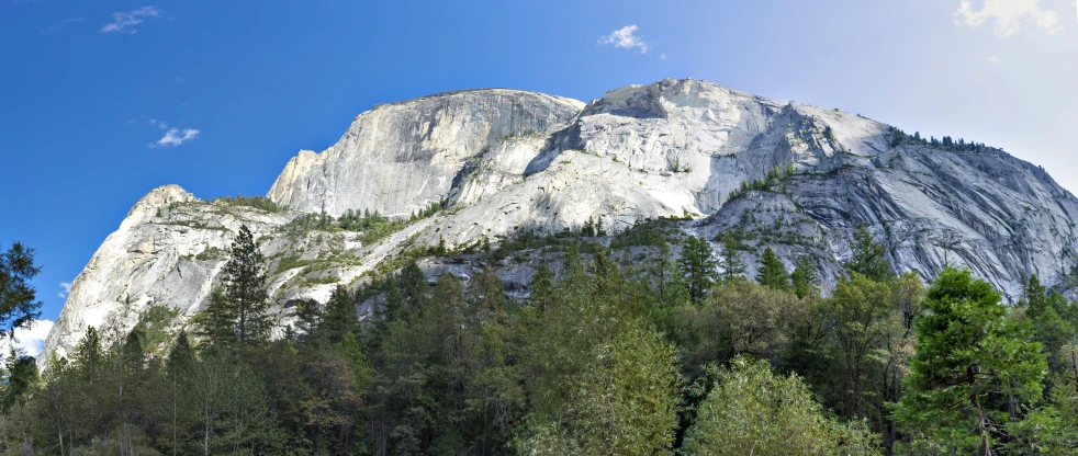 mountain towering over trees and blue sky with clouds