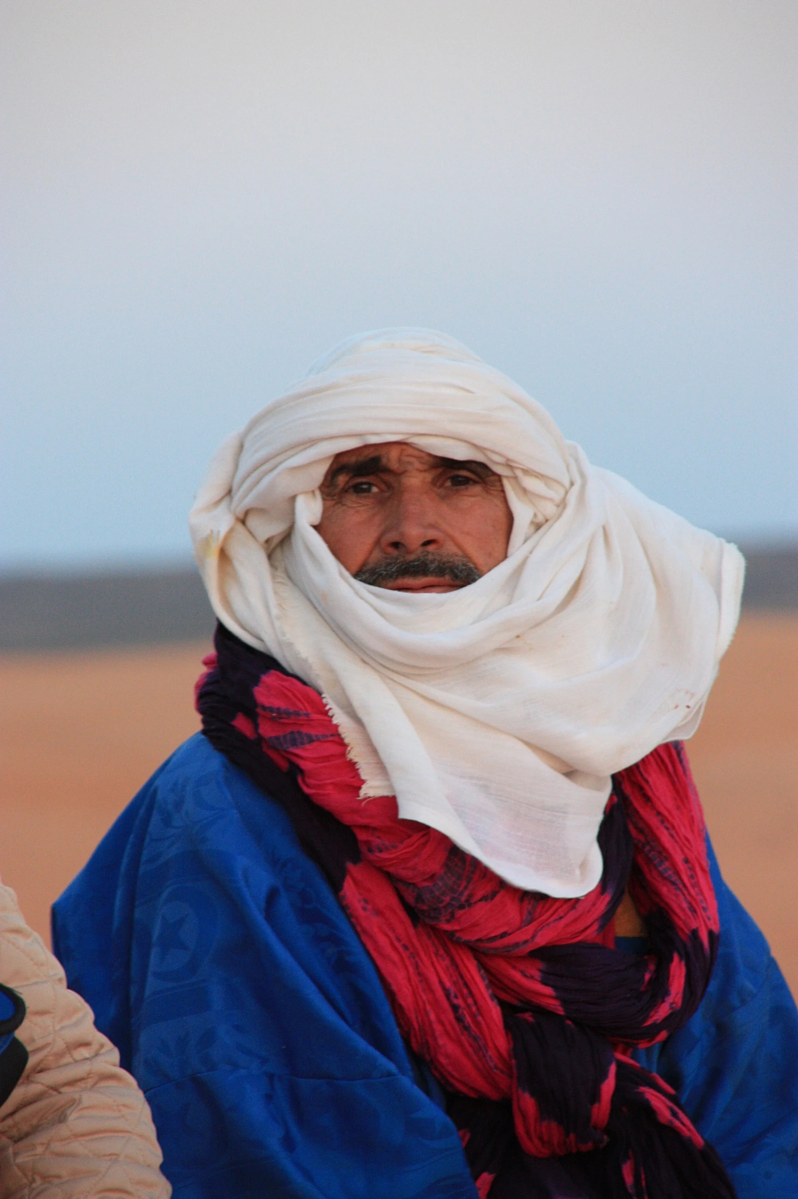 man in white scarf standing on sandy ground