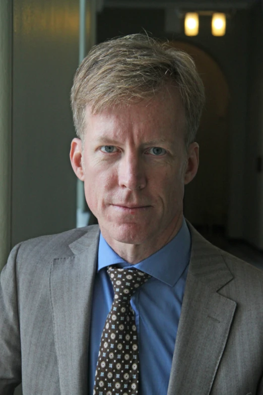 a man with blonde hair and blue eyes poses in a gray suit