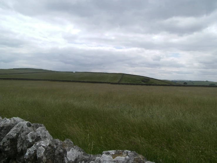 a large grassy field with a stone wall and green hills