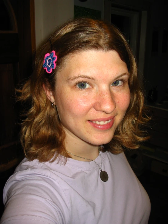 the young woman smiles at the camera, with a pink flower in her hair