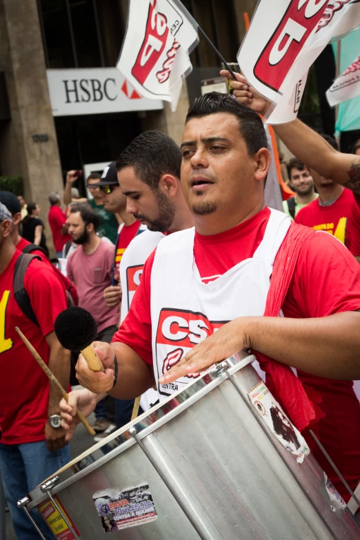 the young man is carrying a silver drum as the other stands with flags