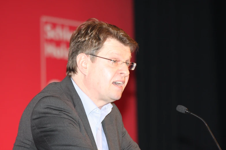 a man sitting at a table speaking at a podium