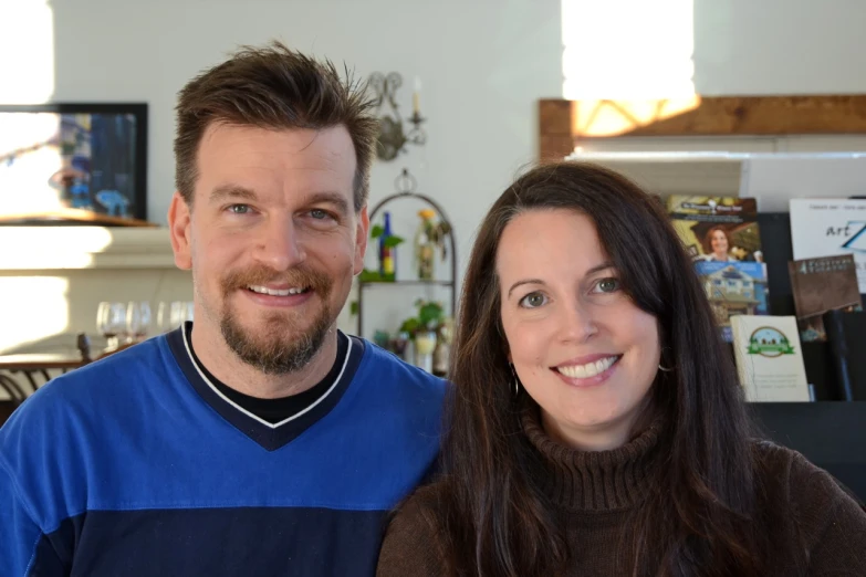 a man and woman smile as they stand in front of a tv