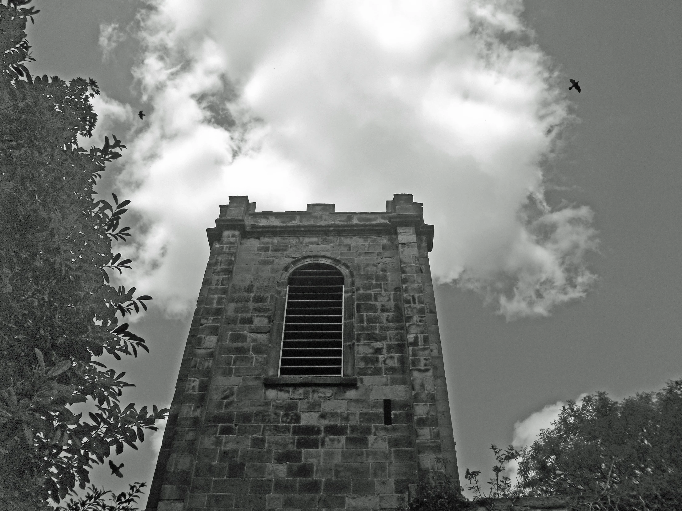 a black and white po shows the side of a tower with clouds above