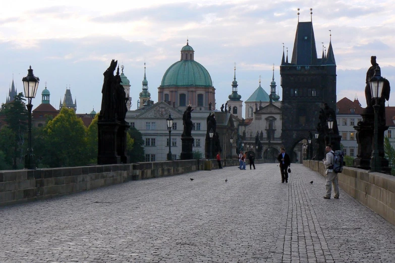 people walk across the cobblestone bridge to a large building