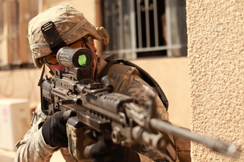 a man in camo shooting a weapon near a building