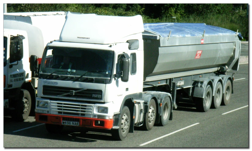 a white truck driving down a street next to a forest