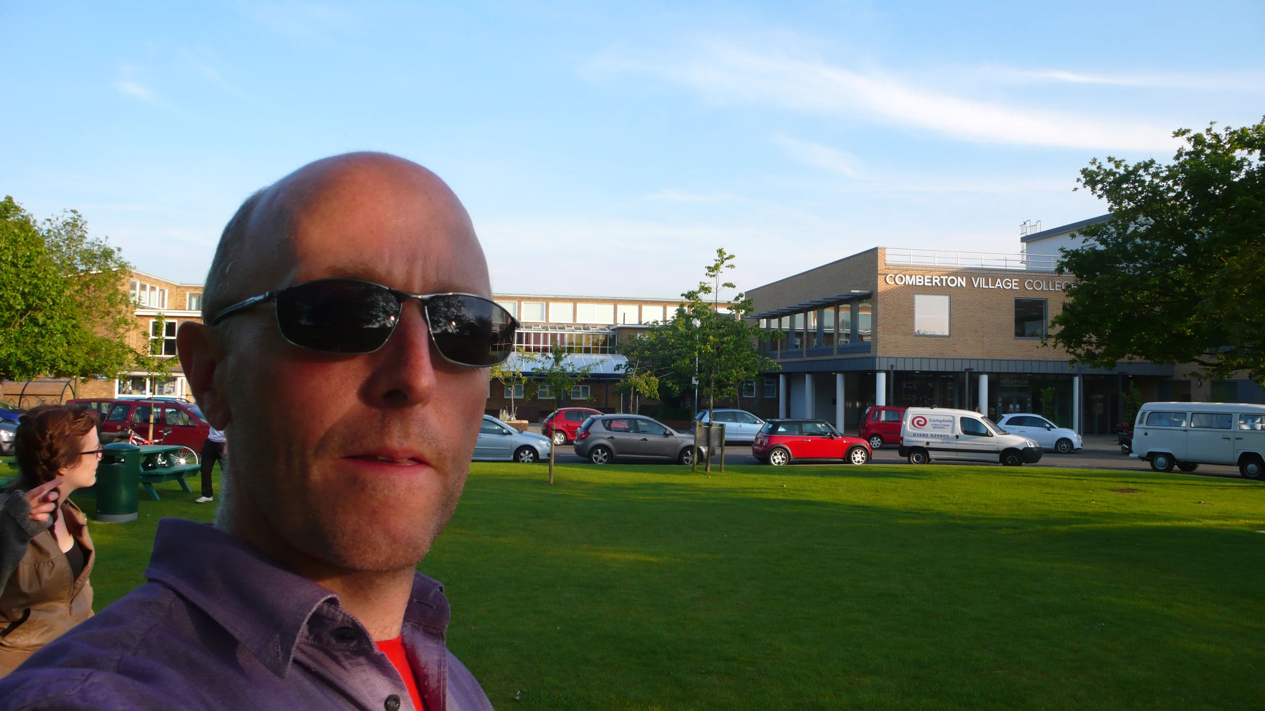 a bald headed man wearing sunglasses standing in front of a row of cars