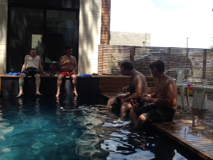 a group of people sit near the pool drinking wine