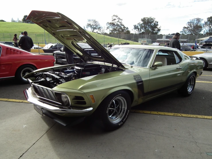 a classic mustang muscle has its hood popped and engine on display at an auto show