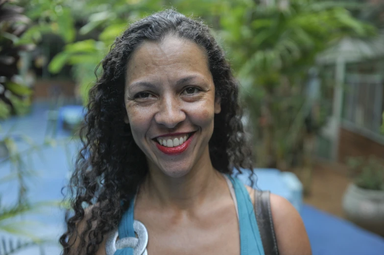 the smiling woman with curly hair is wearing a blue tank top