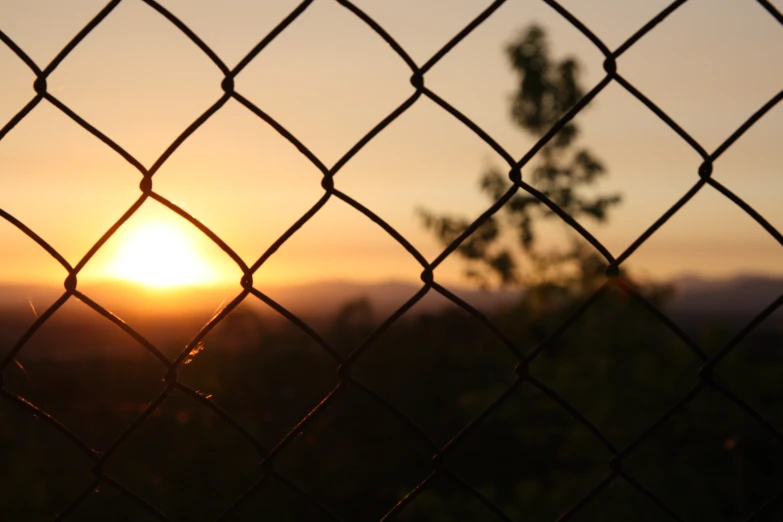 a chain link fence with a sunset behind it