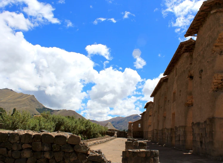 a dirt road going between two buildings with mountains in the background