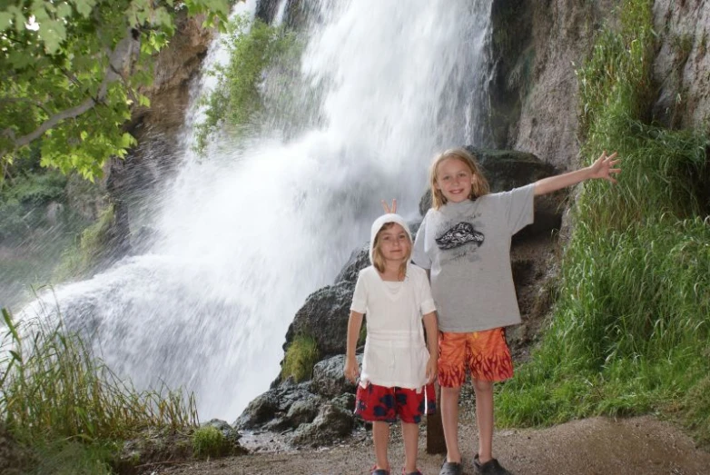 two children stand next to waterfall on path