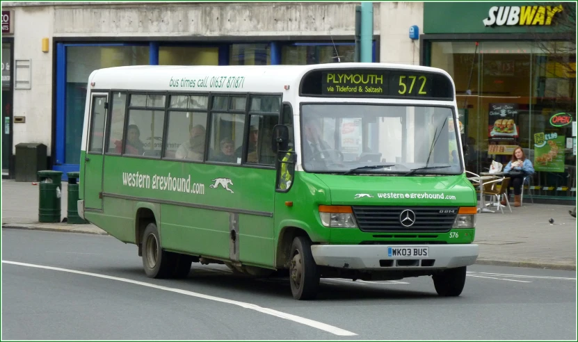 a green bus driving down a street past a store