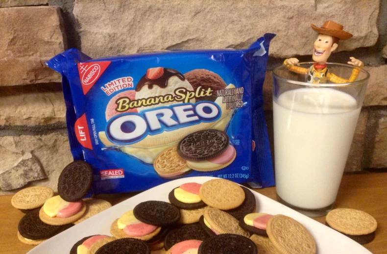 cookies next to a glass of milk, a bag of oreo biscuits and a statue on the table