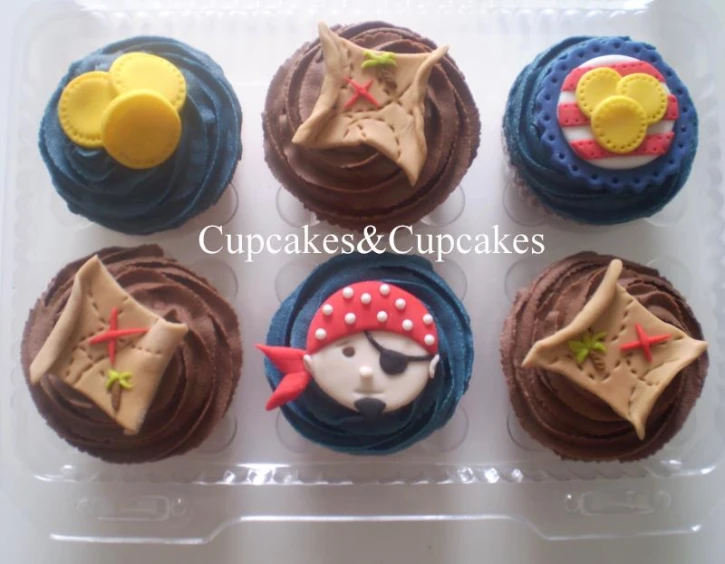 a plastic container with six cupcakes that are decorated like pirate items