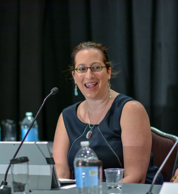 a woman sits behind a microphone in front of a podium