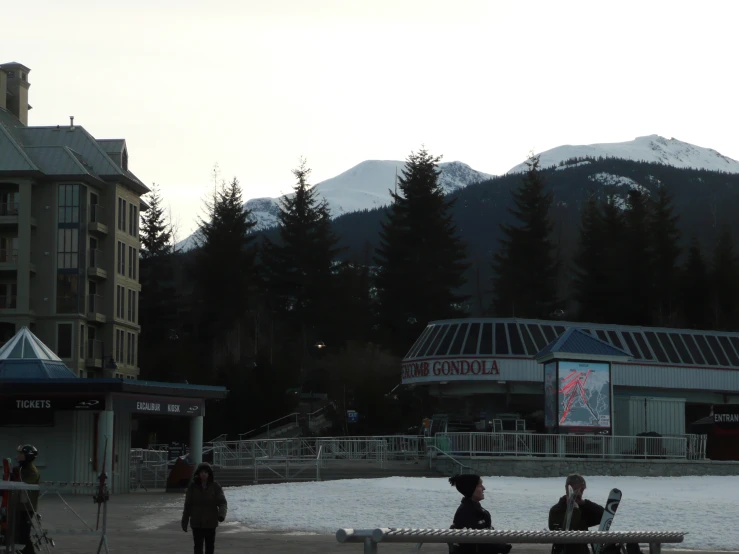 people walking around in front of a building with mountains behind them