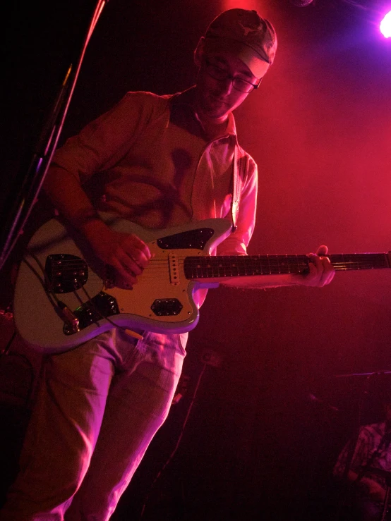 a man playing guitar in front of pink lighting