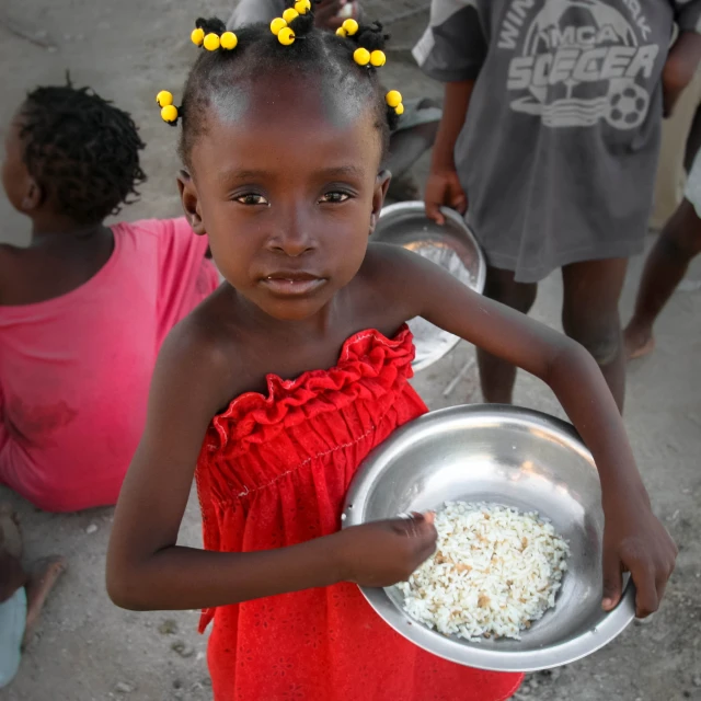 a little girl is standing with a bowl full of rice