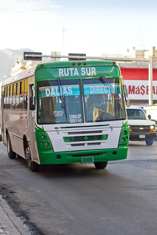 a green bus driving on a street next to a bunch of cars