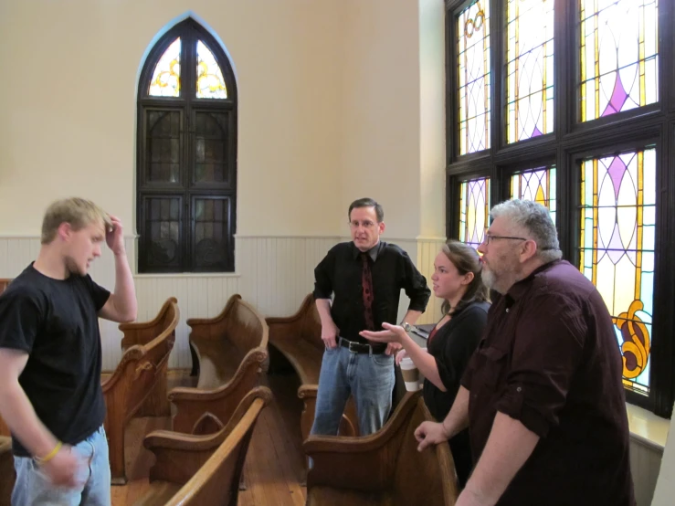 five people stand near wooden pews and look at soing