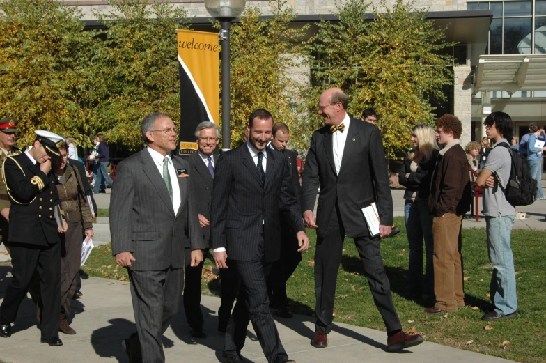 several people dressed in suits and ties and talking on the sidewalk