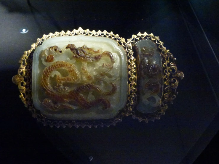 a white and gold dragon design vase sits in a glass box