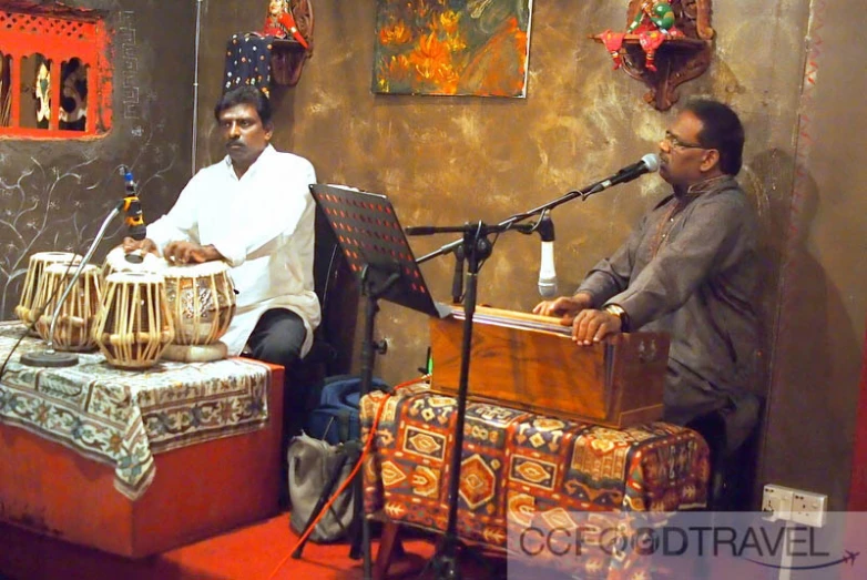 two men sitting at drums on stools in front of microphones