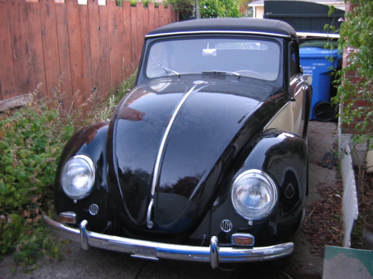 the front view of a black classic car parked next to a wooden fence