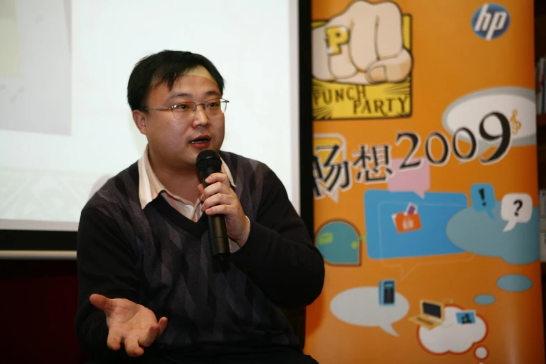 an asian man in glasses speaking into a microphone