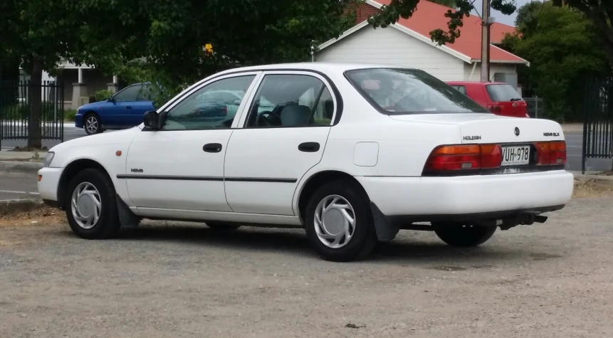 a white car sitting in a parking lot next to a tree