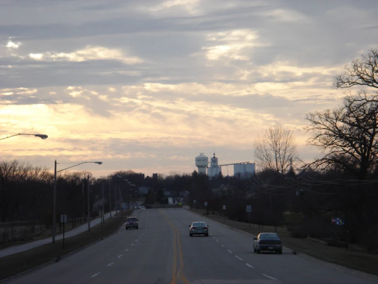 two cars are driving on a street in a sunset