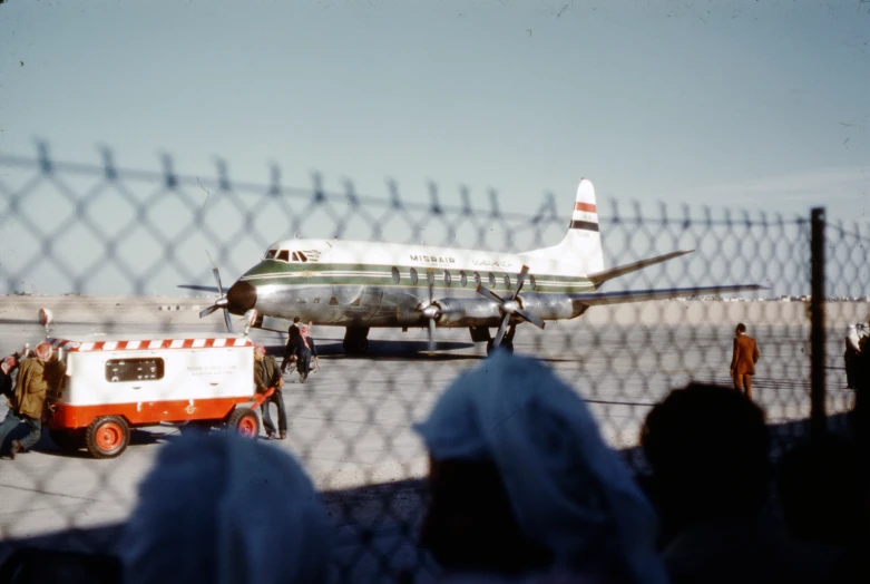 people line up near a fence where an air plane is parked