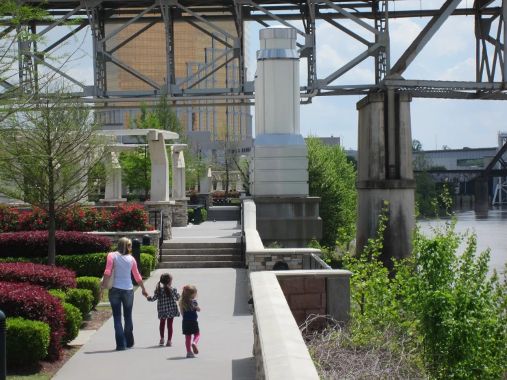 two people, one holding the hand of a child, are walking down a path by some flowers and bushes