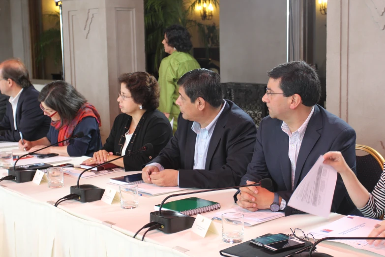 five people seated at a table with papers and remote controls