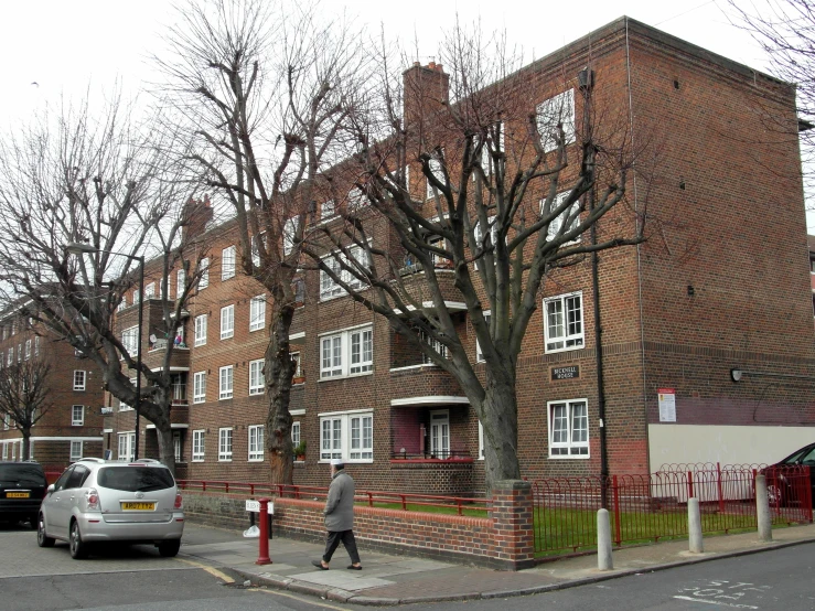 a large brick building with many windows, and several cars parked on the street