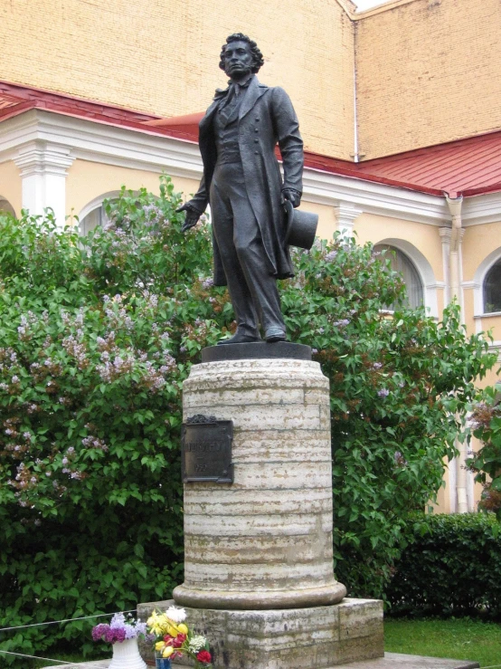 statue of a man on the pedestal in front of trees and bushes