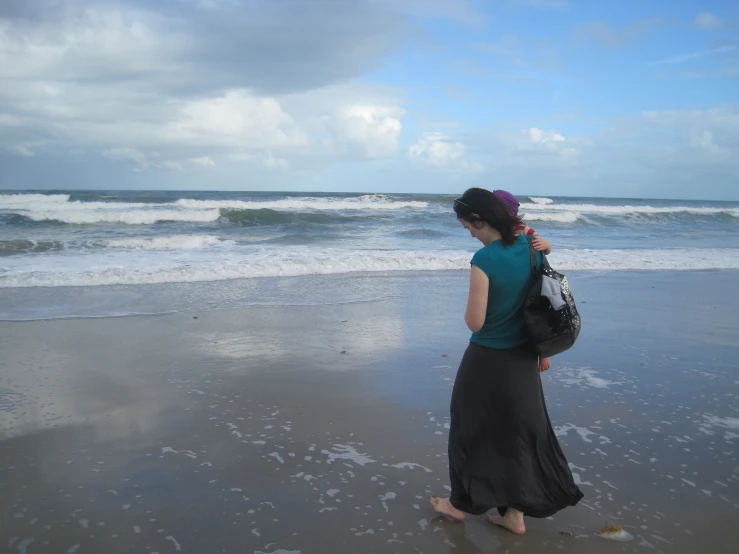 woman in long dress on beach with bags and waves