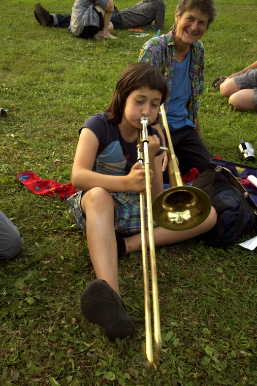 a woman and little girl sitting on the grass playing music