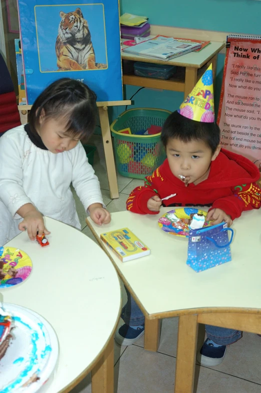 two children in birthday hats sit at the table
